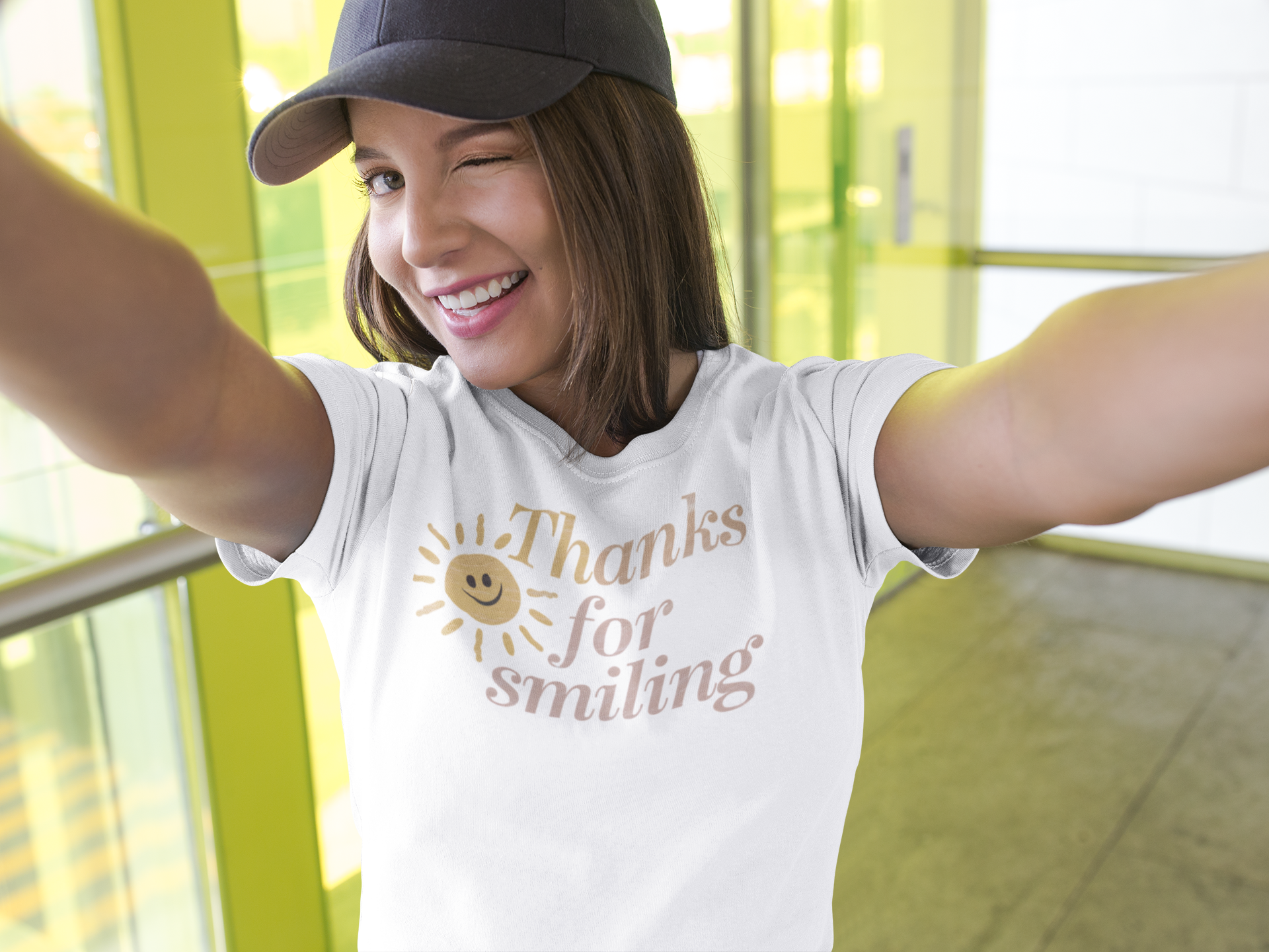 a pretty girl wearing a unisex t-shirt with a smiling sun and the slogan Thanks For Smiling. with a wink and a gift