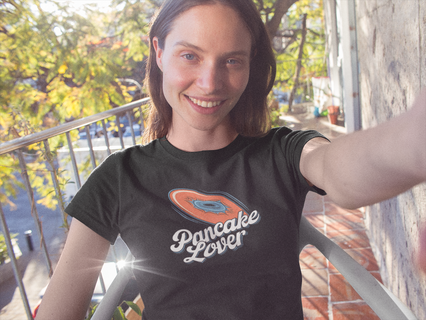 a young woman wearing a black Pancake Lover Ultimate frisbee shirt featuring a flying pancake in retro design lettering