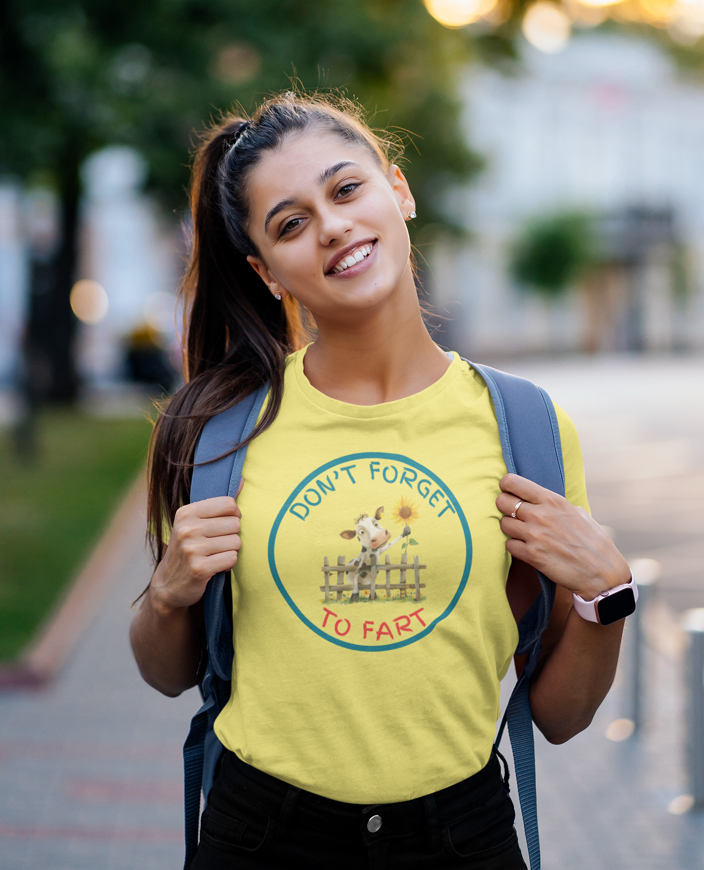 a young woman wearing a t shirt of a cow leaning over a fence holding a flower with the funny caption Don't Forget To Fart