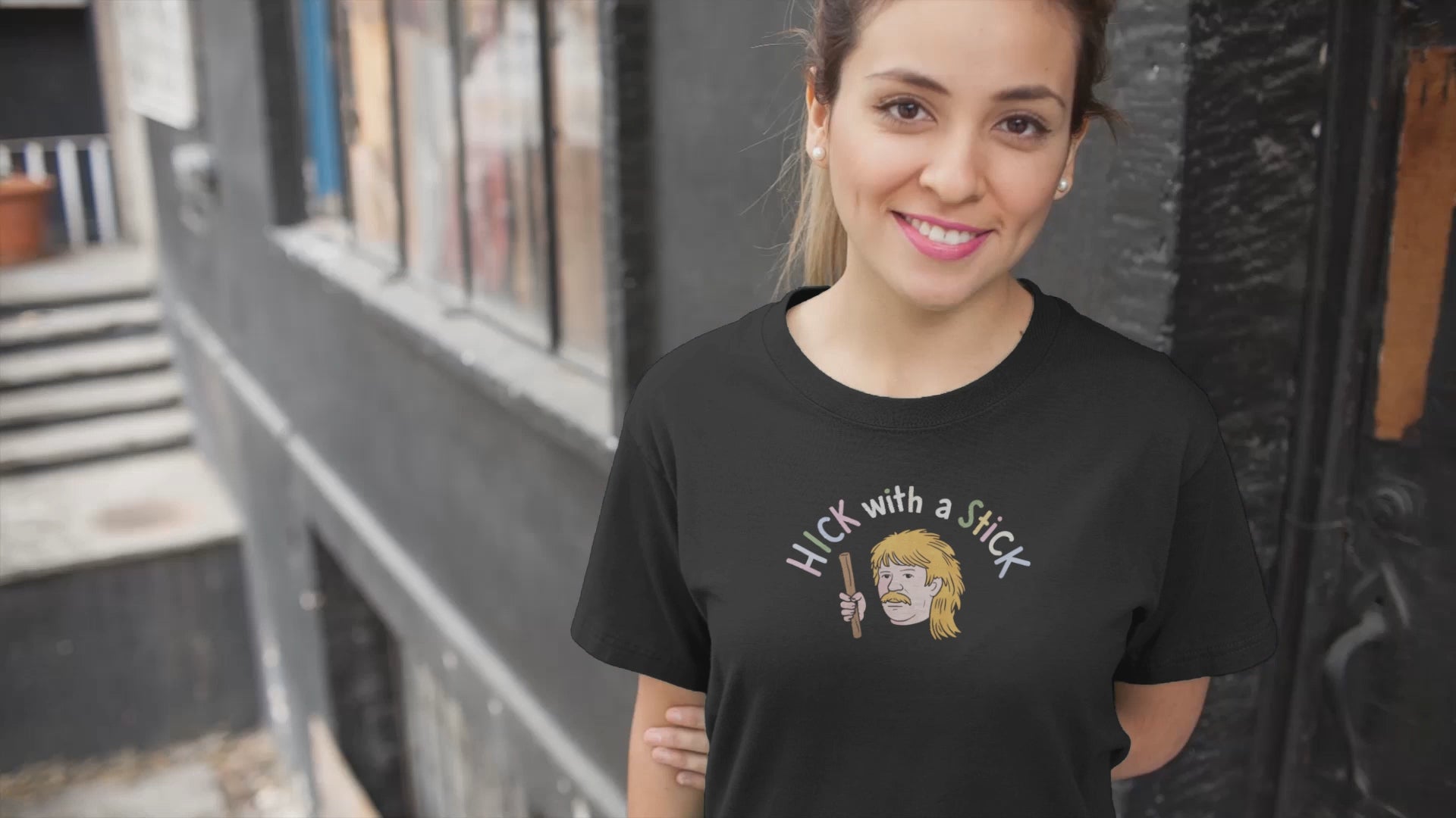 a young woman wearing a shirt with the  illustration of hillbilly with mullet holding a stick with the funny caption Hick with a Stick