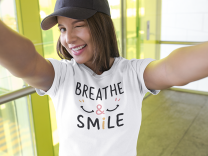 A happy woman wearing a t-shirt with the words "Breathe & Smile"  there are smiling faces on each side of phrase
