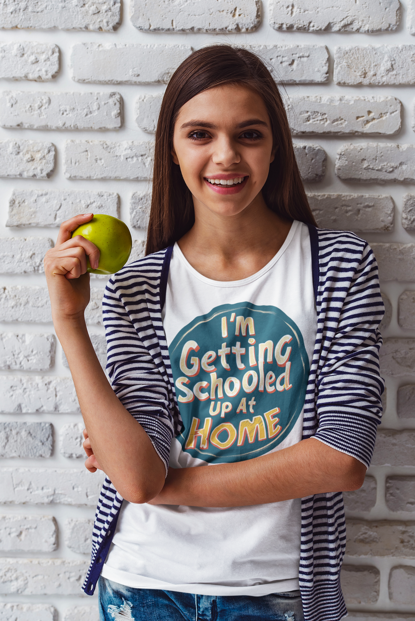 A girl wearing a white t-shirt holding an apple. The shirt has caption is I'm Getting Schooled Up At home