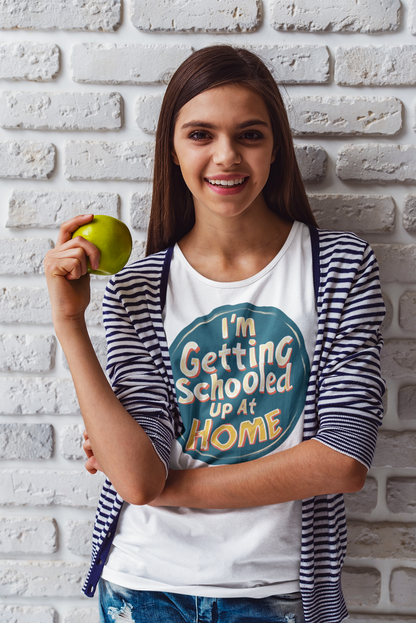 A girl wearing a white t-shirt holding an apple. The shirt has caption is I'm Getting Schooled Up At home