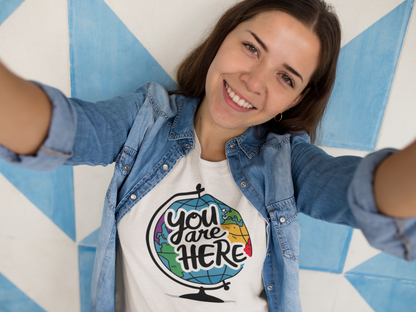 A happy girl wearing a white shirt with the caption You Are Here on top of a spin globe