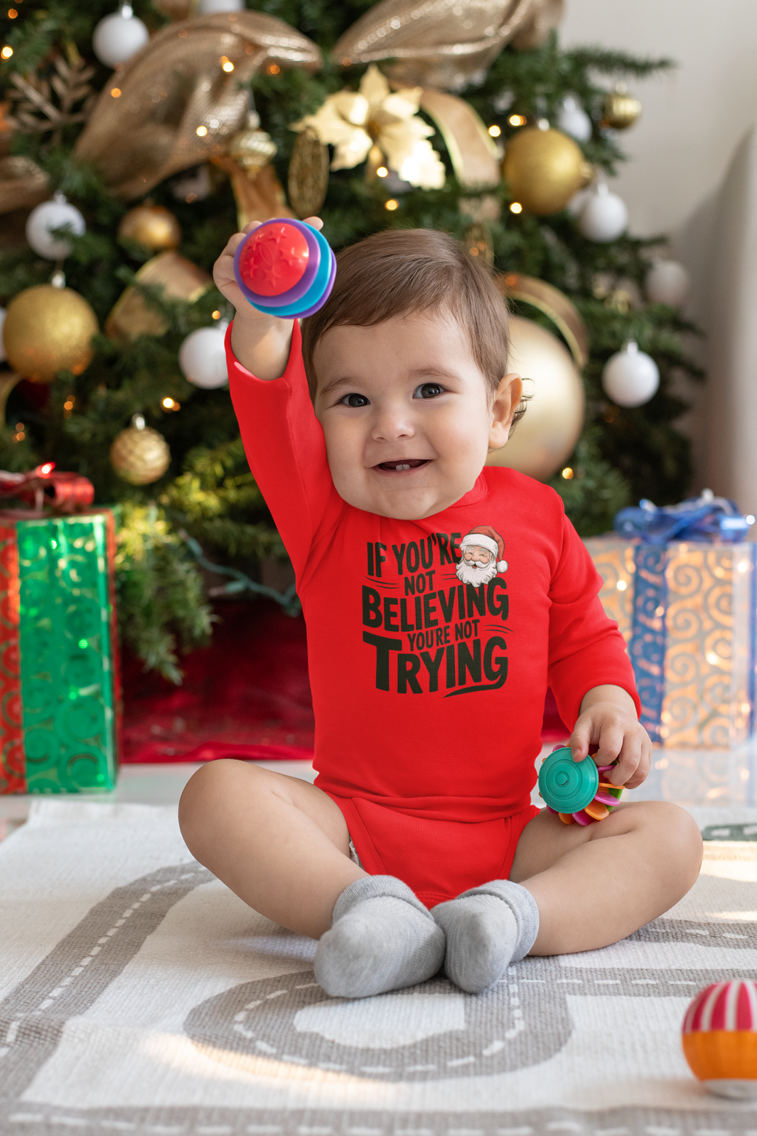 Baby in christmas onesie wearing a If you're not beieving you're not trying gift