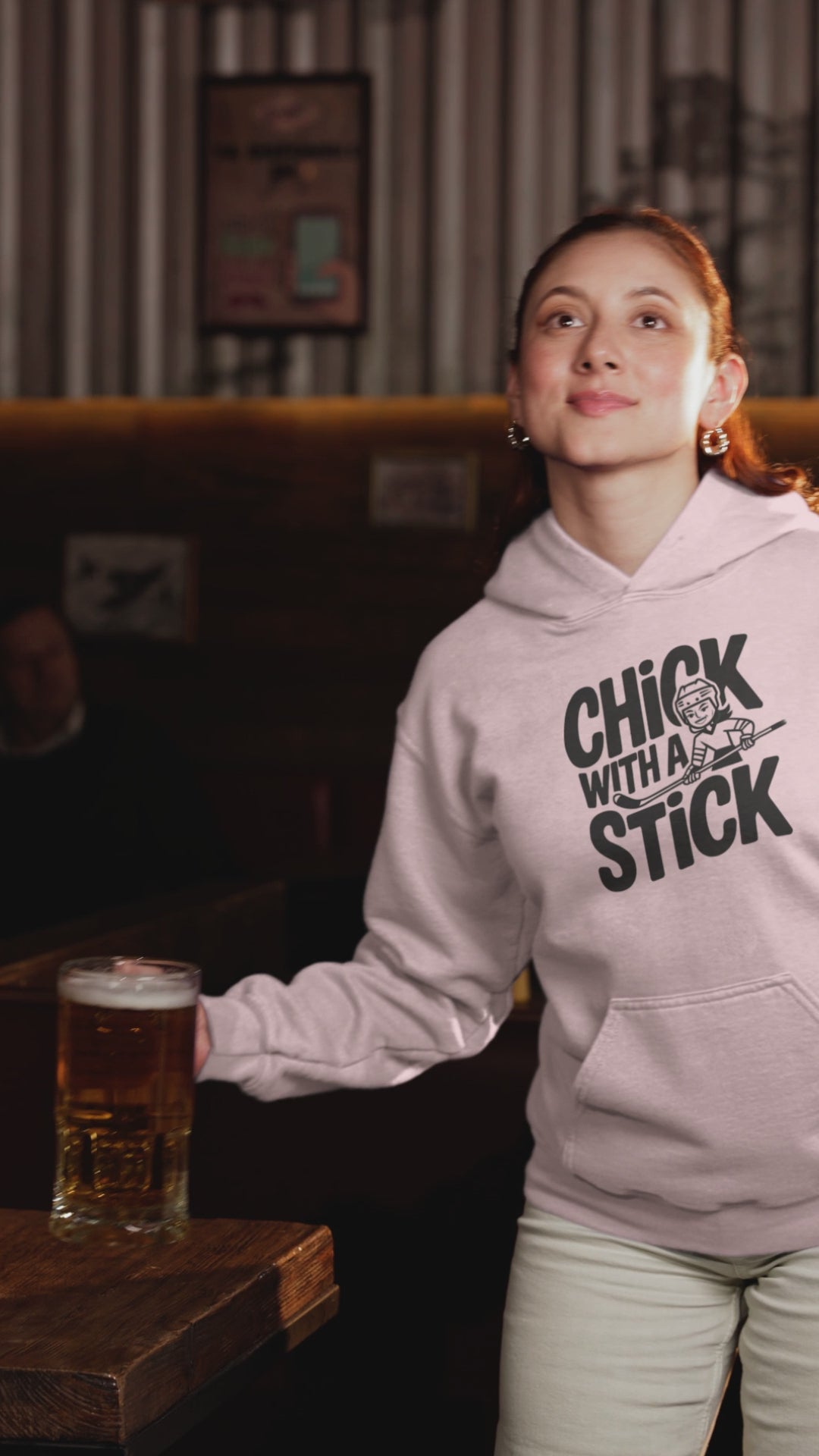A video of woman sporting a hoodies with the hockey slogan Chick With A Stick