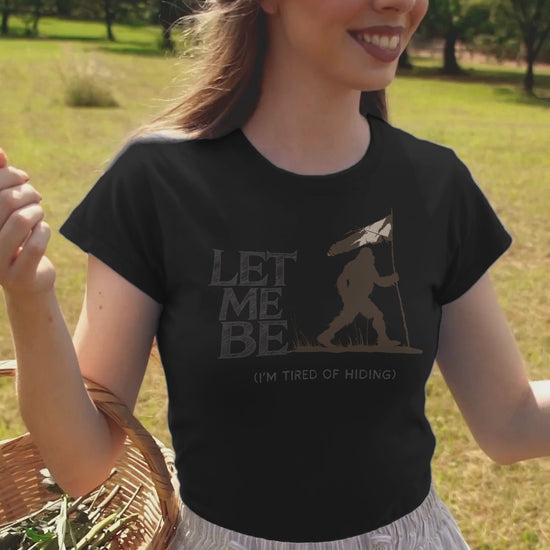 a young woman in video wearing a  t-shirt of bigfoot holding a surronder flag with the caption Let Me Be I'm Tired Of Hiding